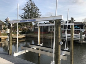 A 4-post aluminum boat lift next to a stationary dock on a canal